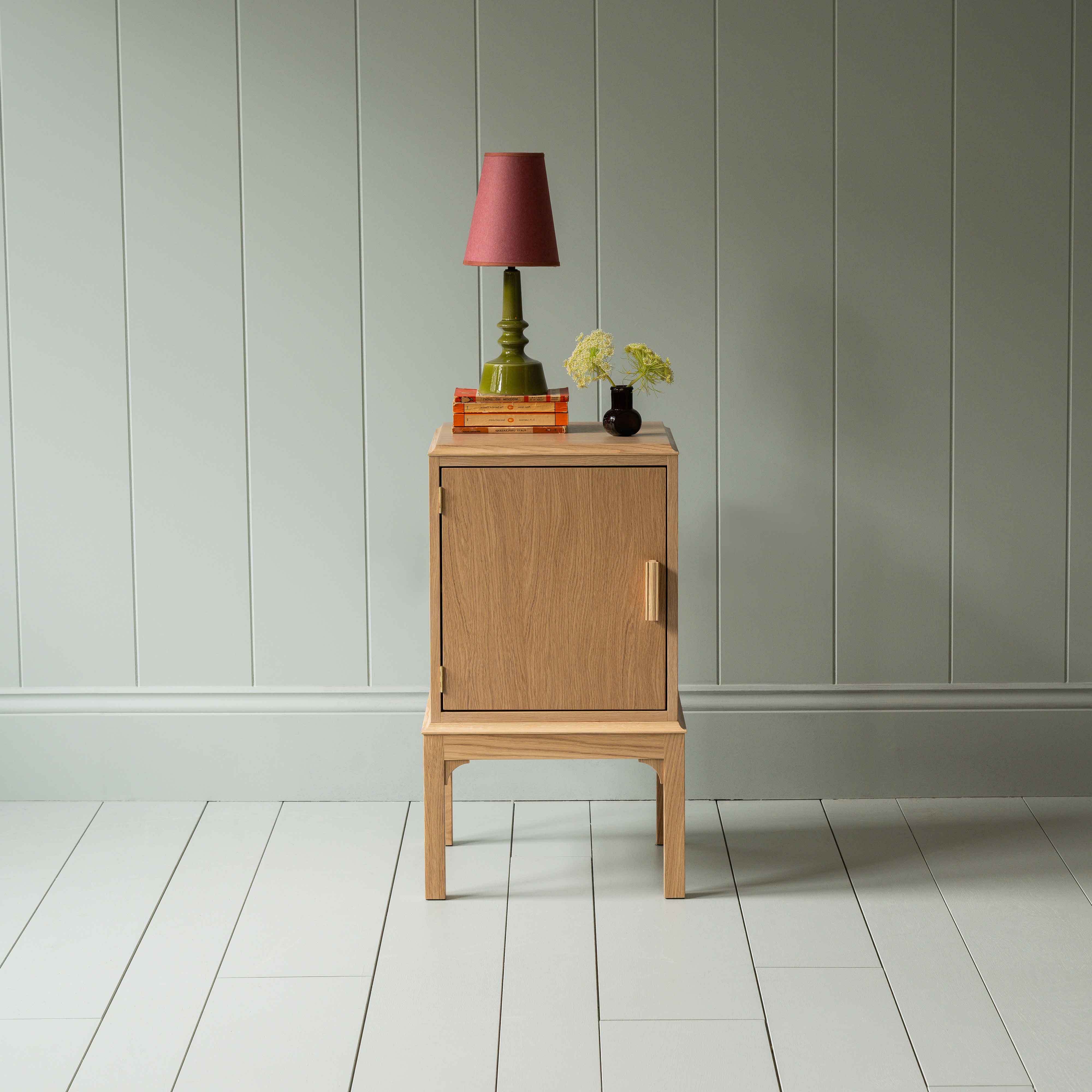 Bits and Bobs Bedside Table, Natural Oak, Left Hand Side Decorated with table lamp and a small bottle of flowers - Nicola Harding & Co.
