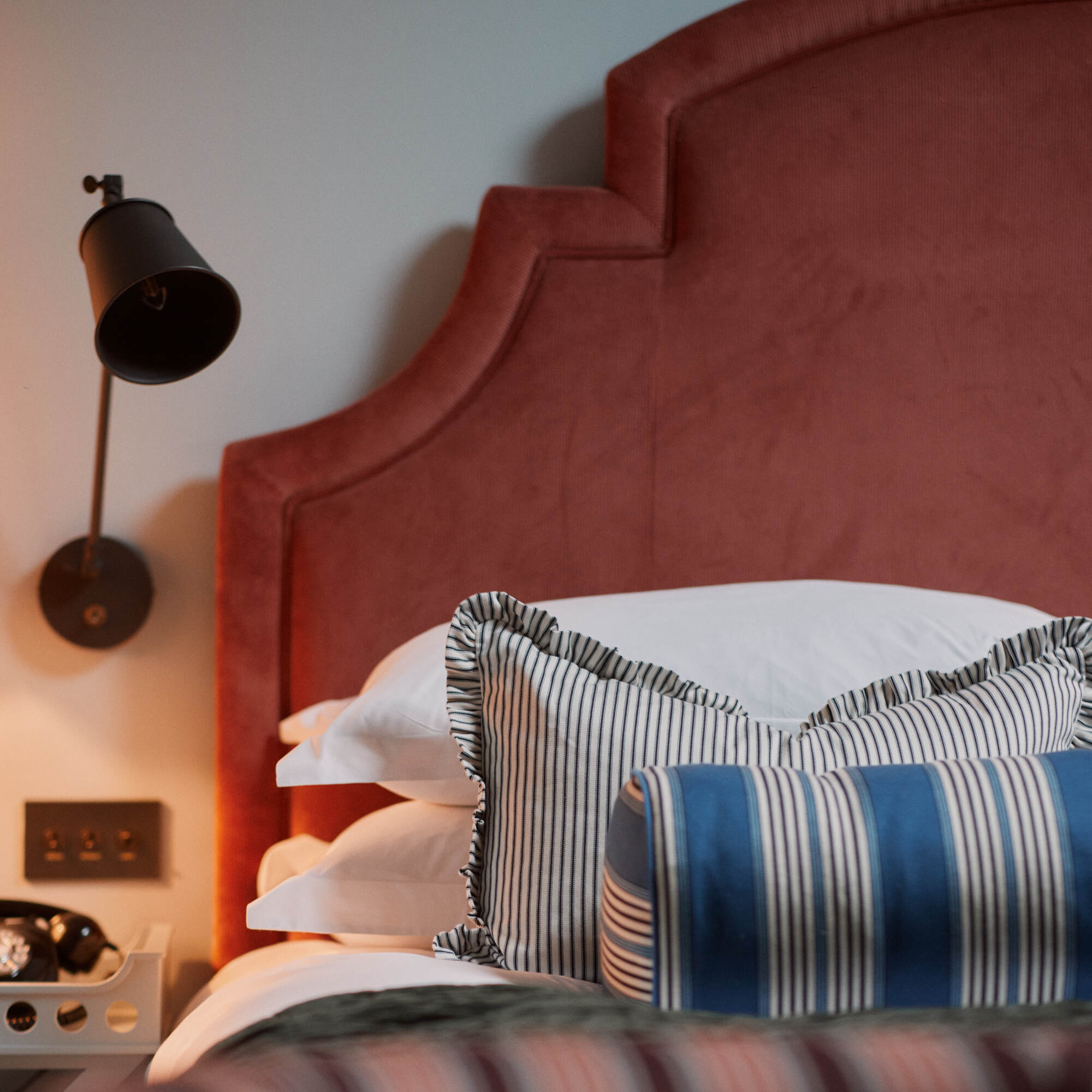 Bed with cushions & pillows and a wall-mounted bedside lamp featuring a waxed brass lampshade Designed By Nicola Harding & Co.