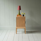 Bits and Bobs Bedside Table, Natural Oak, Left Hand Side Decorated with table lamp and a small bottle of flowers - Nicola Harding & Co.