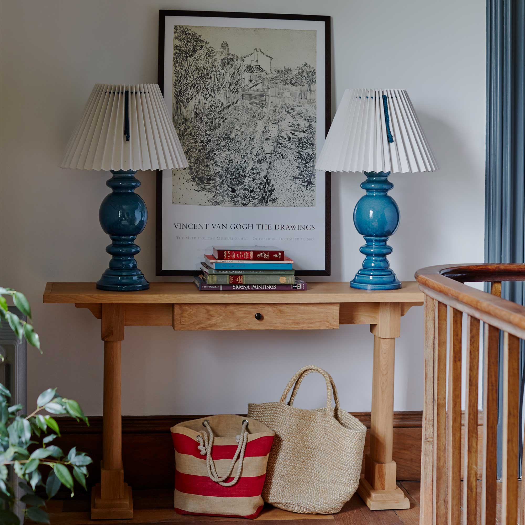  Keepsake Console Table in oiled oak with a drawer, placed in a walkway, adorned with a couple of books and two blue base lamps. 