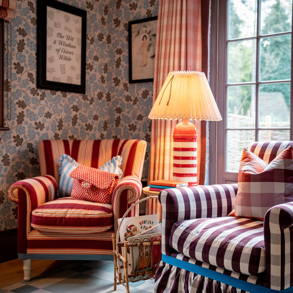 Living room featuring Acorn wallpaper in Sugarbag Blue and Mushroom, with two armchairs, a side table with a cherry red base, a lampshade, and warm lighting.