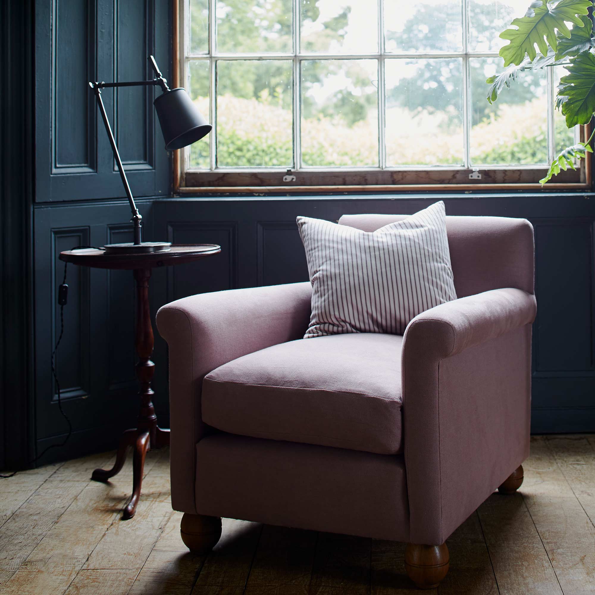  Focused Table Lamp Base in Waxed Brass, With Black Lampshade on a Side Table Next to an Armchair With a Cushion - NiX By Nicola Harding 