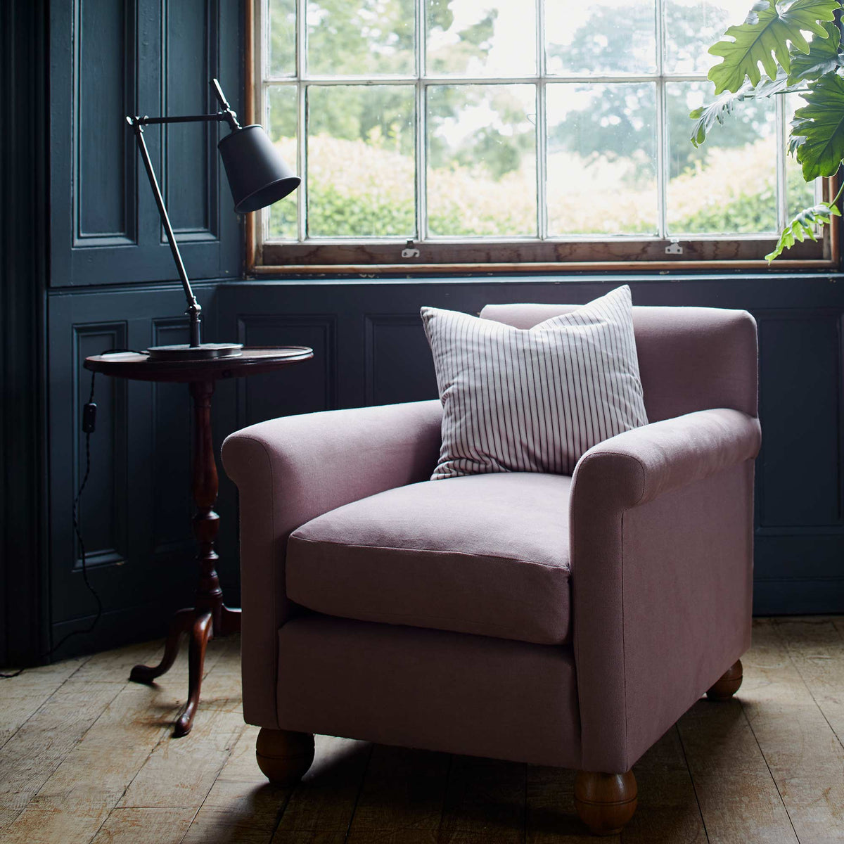 Focused Table Lamp Base in Waxed Brass, With Black Lampshade on a Side Table Next to an Armchair With a Cushion - NiX By Nicola Harding