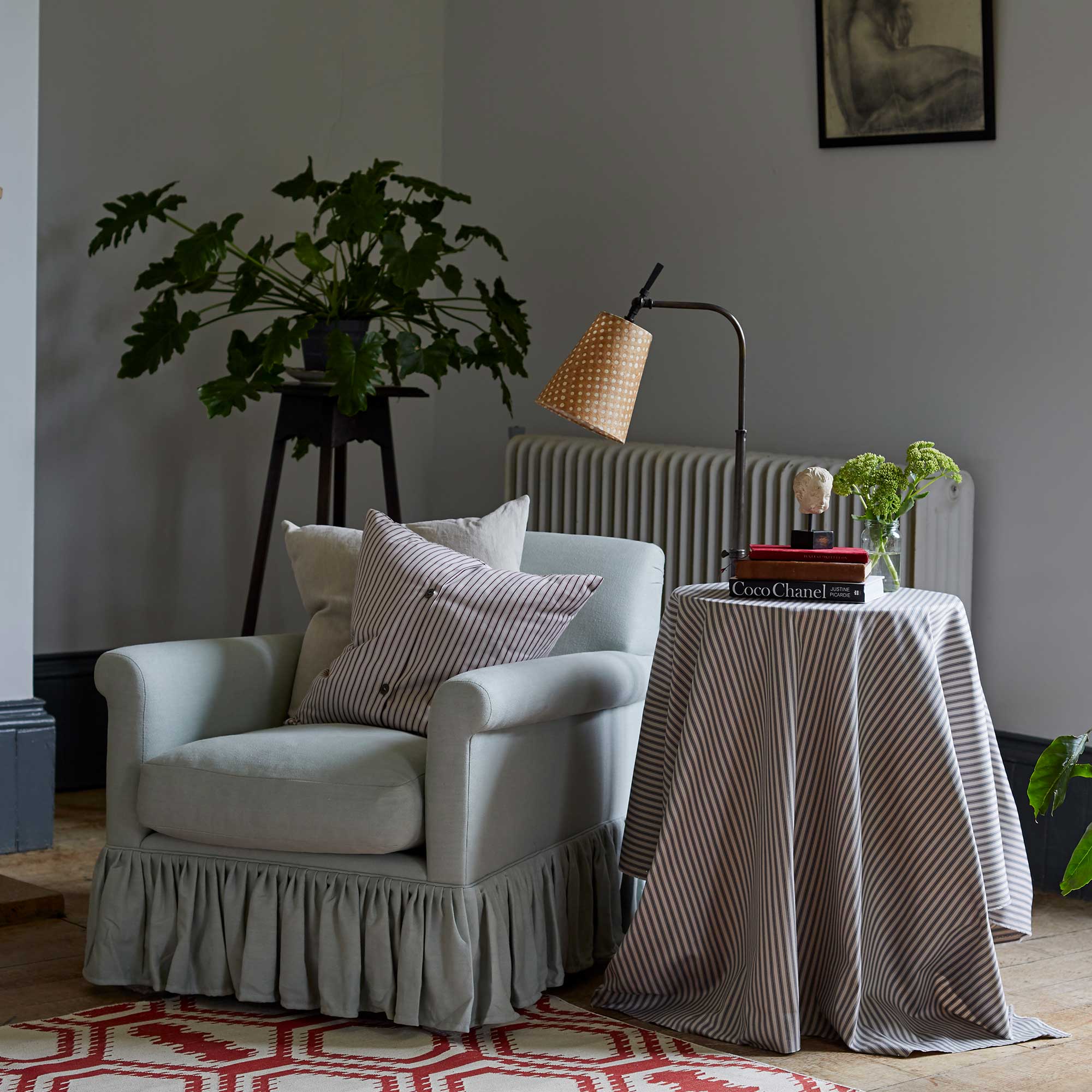  To The Point Floor Lamp Base in Waxed Brass, With Dotted Lampshade Next to a Side Table and an Curtain Call Arm Chair With 2 NiX Cushions - By NiX 