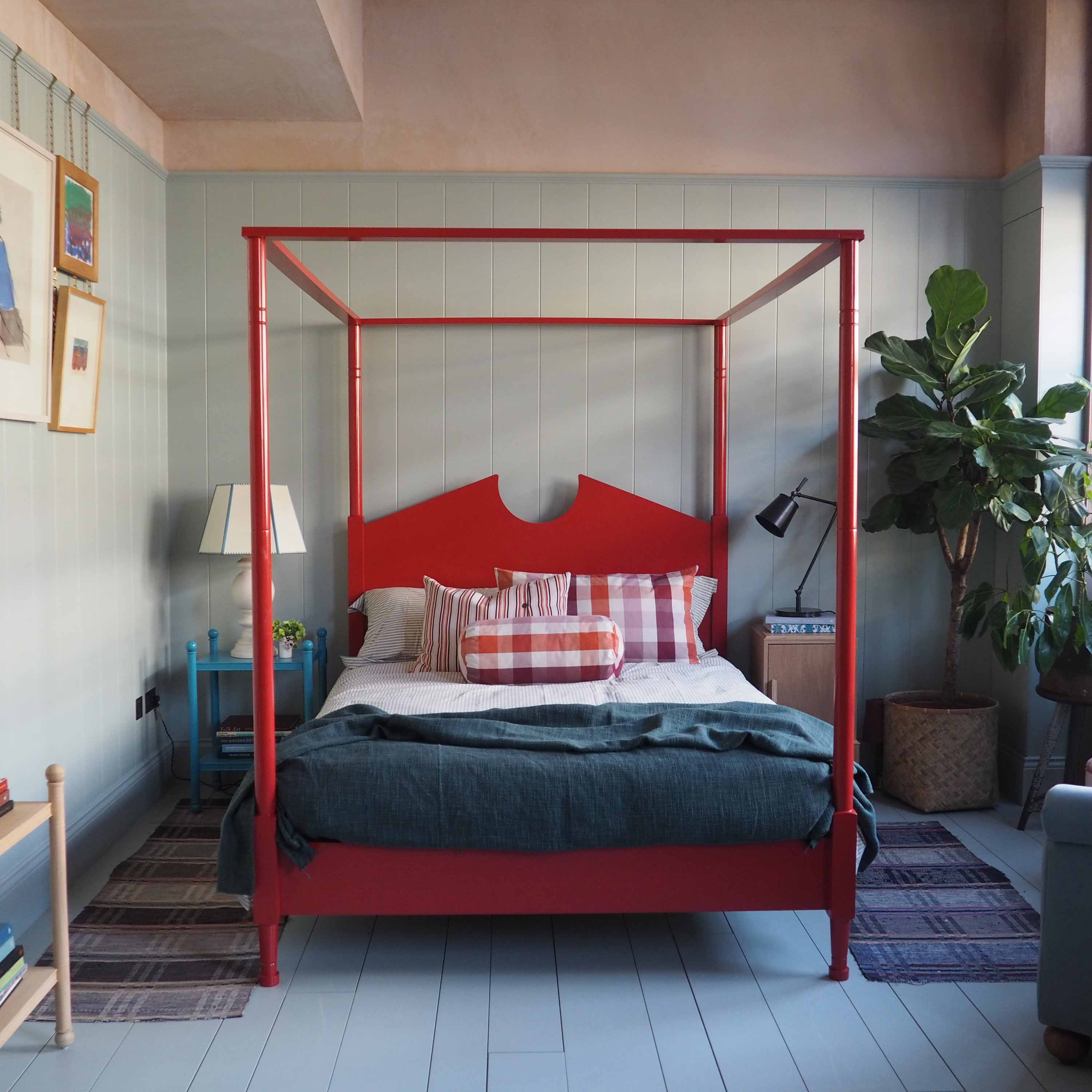  Red four-poster bed in a beautifully decorated bedroom with side tables, plants, and lamps by Nicola Harding & Co. 