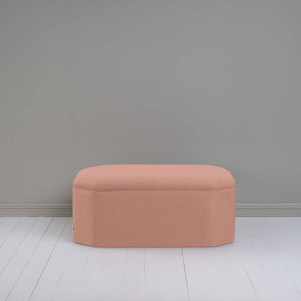 A small light pink ottoman, perfect for adding a touch of color and comfort to any room.