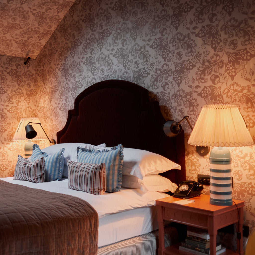  Bedroom decorated with Albion wallpaper in Mauve on the walls, featuring warm lighting and table lamps. 