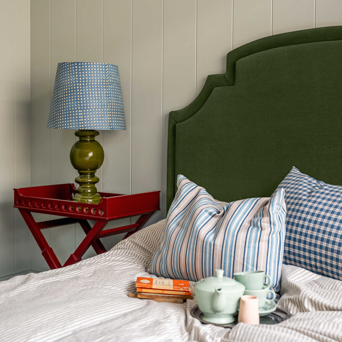 Seventh Heaven Upholstered Bed in Intelligent Velvet Juniper without Valance, featuring a red side table with a lamp, books, and a teapot with cups on the bed, along with pillows.