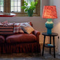  Humbug Straight Empire Batik Paper Lampshade in Dotty Maroon with Hourglass Ceramic Table Lamp Base in Blue, Lights 'ON,' Next to NiX 4-Seater Sofa and Spindle Side Table in Carbon Black – Nicola Harding 