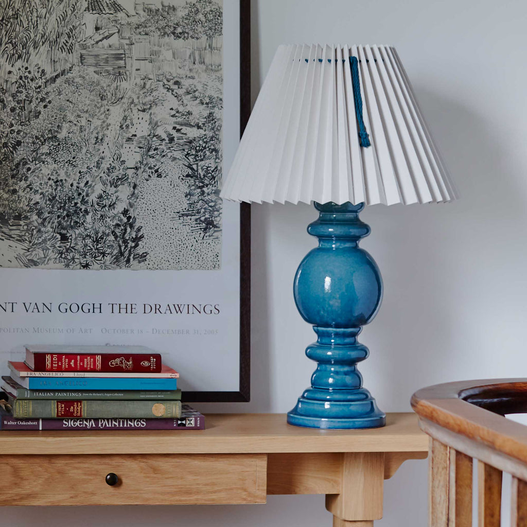  Sunburst Concertina Natural Pleat Lamp Shade with Peacock Blue Cord, With Hourglass Ceramic Table Lamp Base in Blue, On a Keepsake Console Table, Oiled Oak With Bunch of Books and a painting on the Wall - By NiX 