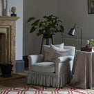 Nicola Harding interiors Curtain Call armchair with a gathered skirt styled next to a fireplace and a draped fabric on side table