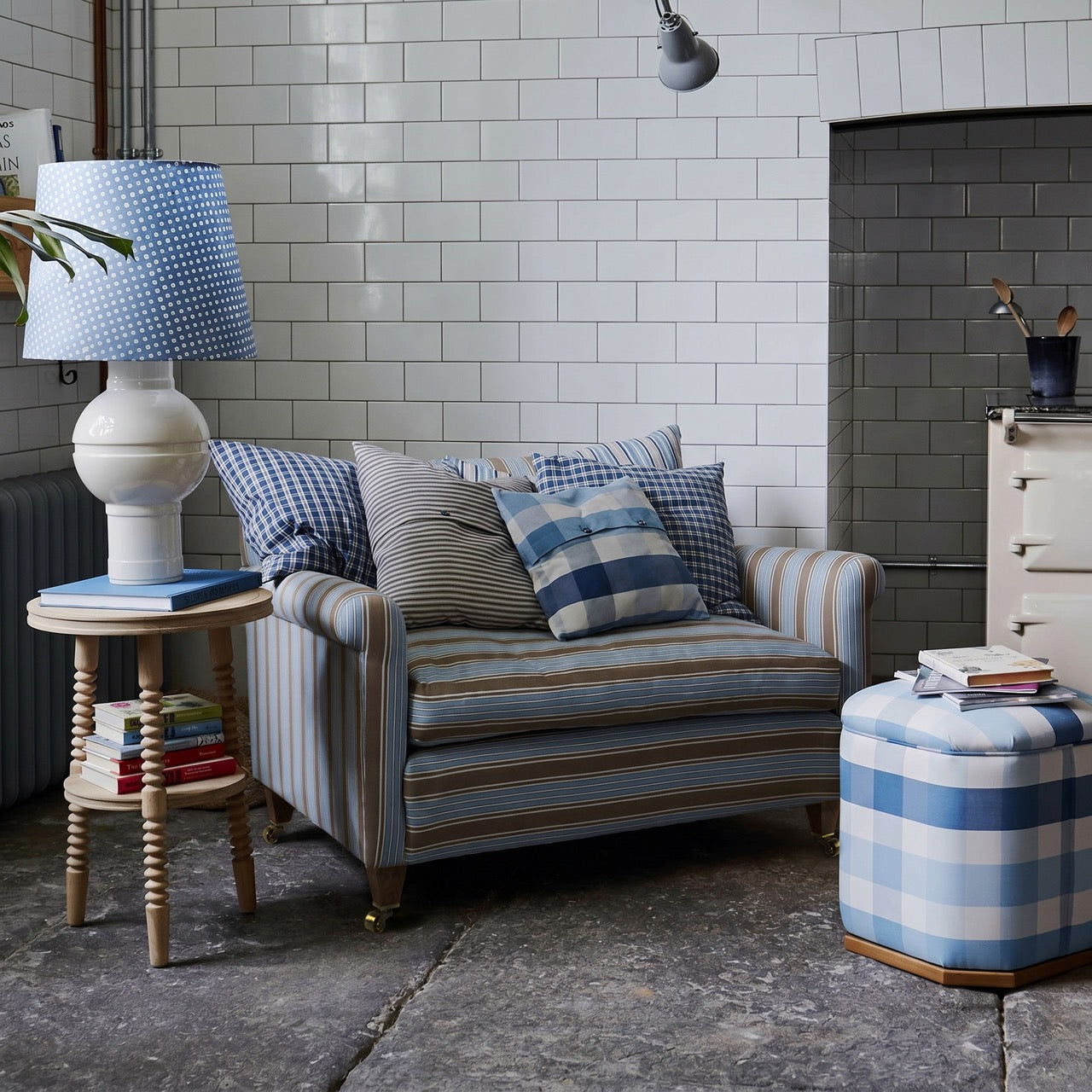  Nicola Harding interiors striped love seat sofa styled with a blue cushion and a ceramic table lamp in a kitchen setting. 
