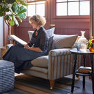 Nicola Harding of Nicola Harding interiors reading a book on a striped love seat sofa next to a bobbin side table