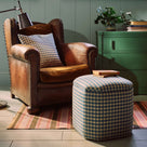 Nicola Harding interiors checkered upholstered ottoman and footstool styled next to a vintage leather armchair