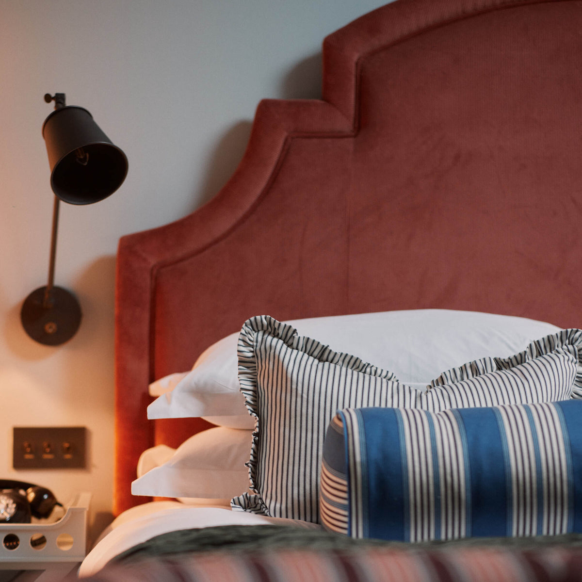 Bed with cushions & pillows and a wall-mounted bedside lamp featuring a waxed brass lampshade Designed By Nicola Harding & Co.