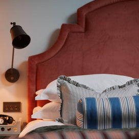 Bed with cushions & pillows and a wall-mounted bedside lamp featuring a waxed brass lampshade Designed By Nicola Harding & Co.