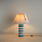Humbug Striped Ceramic Table Lamp Base in Blue & Warm White With Sunburst Concertina Natural Pleat Lamp Shade with Peacock Blackberry  Cord, With Lights 'ON' - Nicola Harding