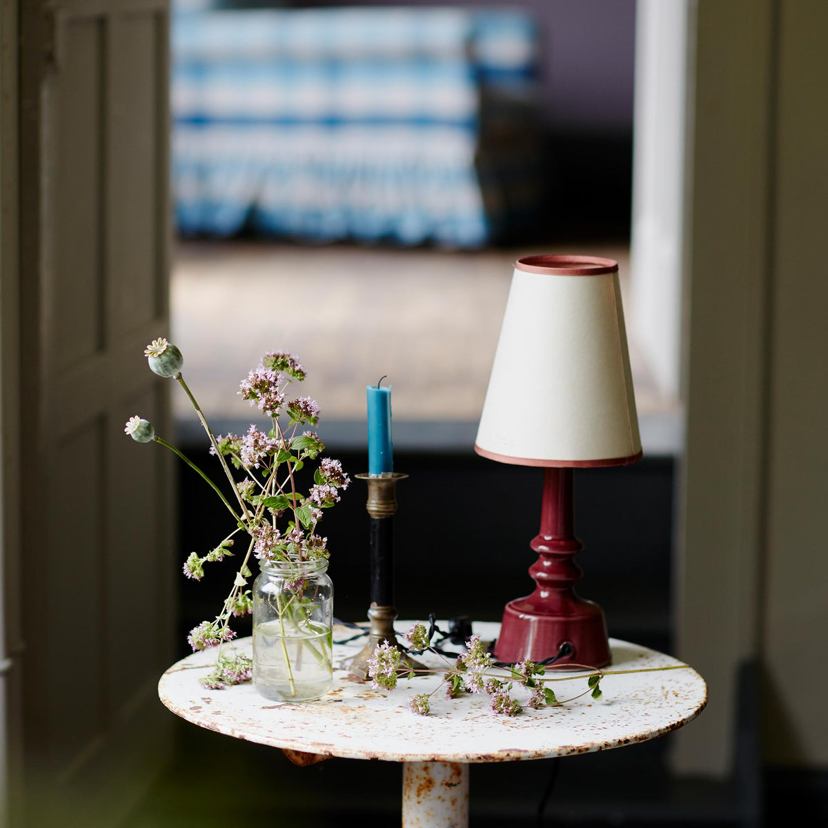 Ditsy Ceramic Table Lamp Base in Damson Pink, With Bright Spark Tall Tapered Paper Lamp Shade in Soft White, a Candle and Bunch of Flowers - Nicola Harding