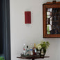  Stitch In Time Wall Light in Burgundy with Muted Pink Trim, Hanging Above a Bunch of Liquor Bottles and a Beautiful Plant – By NiX 
